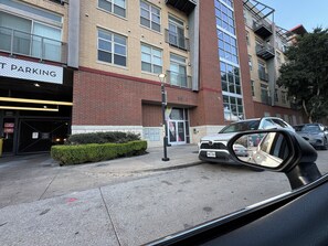 A multi-story building with a parking garage entrance, a leasing office, and a car parked in front. - Cozy 1-bedroom loft apartment Downtown Dallas, gym access and nice pool (Dallas)