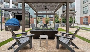 An outdoor patio area with a fire pit, two Adirondack chairs, and a covered grill. - Cozy 1-bedroom loft apartment Downtown Dallas, gym access and nice pool (Dallas)