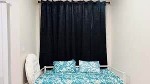 Un dormitorio con una cama, una silla blanca y una cortina oscura.