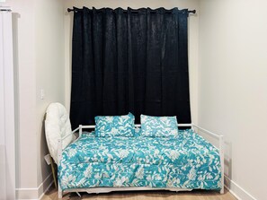 Ein Schlafzimmer mit einem Bett, einem weißen Stuhl und einem dunklen Vorhang.