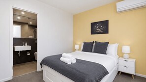 Ein Hotelzimmer mit einem Bett, Nachttischen, einem Badezimmer mit Waschbecken und einem Bild an der Wand.