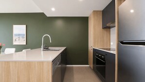 A modern kitchen with a central island, stainless steel appliances, and a green accent wall. - The Lakeview on Grazier (Belconnen)