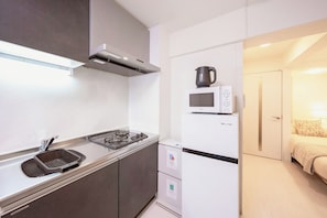 A compact kitchenette with a gas stove, sink, microwave, and a small refrigerator. - Hotel BB (Ota City)