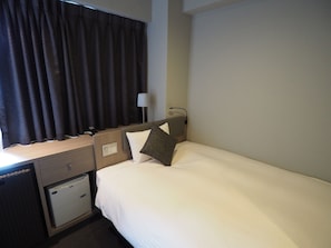 Ein Hotelzimmer mit Bett, Schreibtisch mit Lampe, kleiner Kommode und Fenster mit Vorhängen.