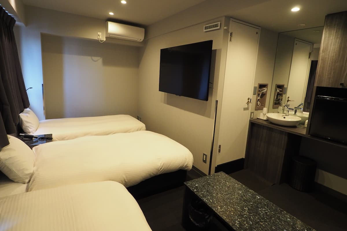 Ein Hotelzimmer mit zwei Betten, einem Flachbildfernseher, einem Badezimmer mit Waschbecken und Spiegel sowie einer Klimaanlage.