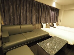 Quarto de hotel moderno com sofá, cama e uma mesa pequena.