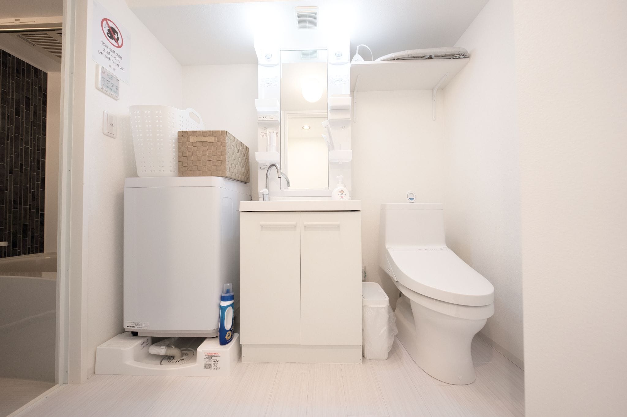 A compact, modern bathroom with a white sink, toilet, and a built-in washing machine.