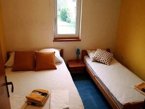 Ein kleines Zimmer mit zwei Einzelbetten, einem Nachttisch, einer Lampe und einem Fenster.