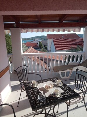 Ein Balkon mit Tisch für zwei Personen, Stühlen und Blick auf Häuser mit roten Dächern.
