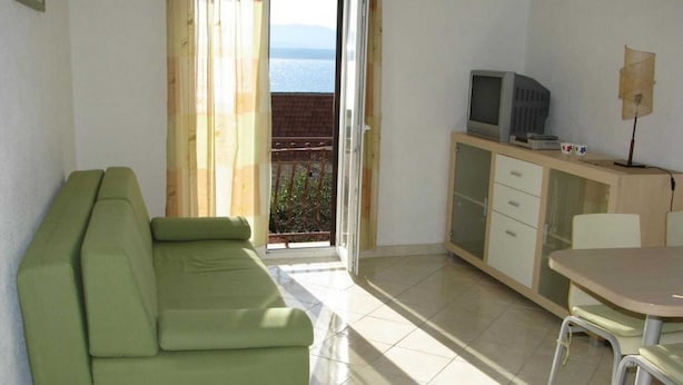 Una habitación con un sofá verde, una mesa pequeña, un televisor y un balcón con vistas.