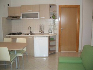 A compact kitchen with a stove, sink, and a small refrigerator. There is a dining table with chairs and a green sofa in the living area. - Apartments Paloc - Standard One-bedroom Apartment With Balcony (Bol)