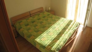 Una cama individual con colcha en una habitación con suelo de madera y ventana con cortinas.