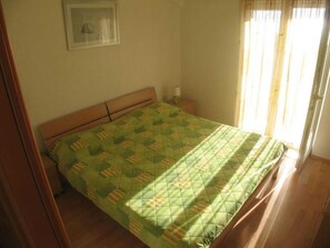 A single bed with a quilt in a room with a wooden floor and a window with curtains. - Apartments Paloc - Standard One-bedroom Apartment With Balcony (Bol)