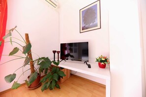 A room with a mounted TV, a potted plant, a framed picture on the wall, and a small red flower pot. - Apartments Melita - Comfort Two Bedroom Apartment With Terrace and Sea View (Zadar)
