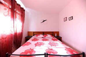A bedroom with a bed, a nightstand, a wall-mounted picture, and a window with curtains. - Apartments Melita - Comfort Two Bedroom Apartment With Terrace and Sea View (Zadar)