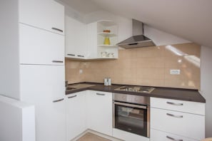 A compact kitchen with white cabinetry, a stove, and a range hood. - Apartments Nina - One-bedroom Apartment (Dubrovnik)