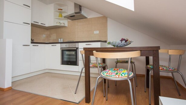 Een moderne keuken met witte kasten, een inbouwoven en een eethoek met een houten tafel en kleurrijke stoelen.