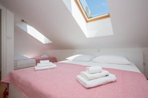 A bedroom with a skylight, a bed with white linens, and a pink striped area rug. - Apartments Nina - One-bedroom Apartment (Dubrovnik)