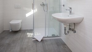 Een moderne badkamer met een glazen douchecabine, een wit wastafelmeubel en een toilet.