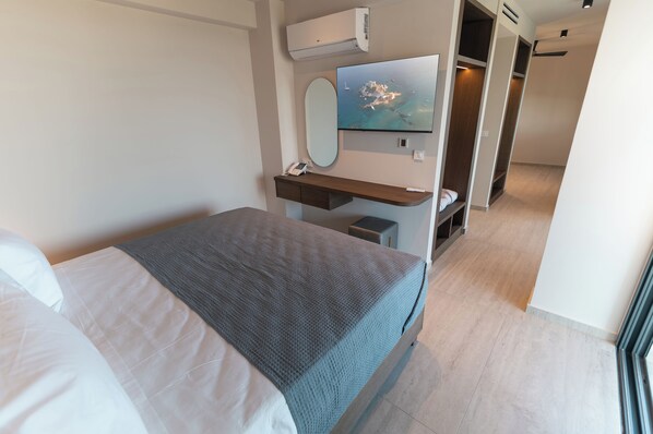 A modern hotel room with a bed, a desk, a mirror, a television, and a view of the sea. - Kefalos View (Kos)