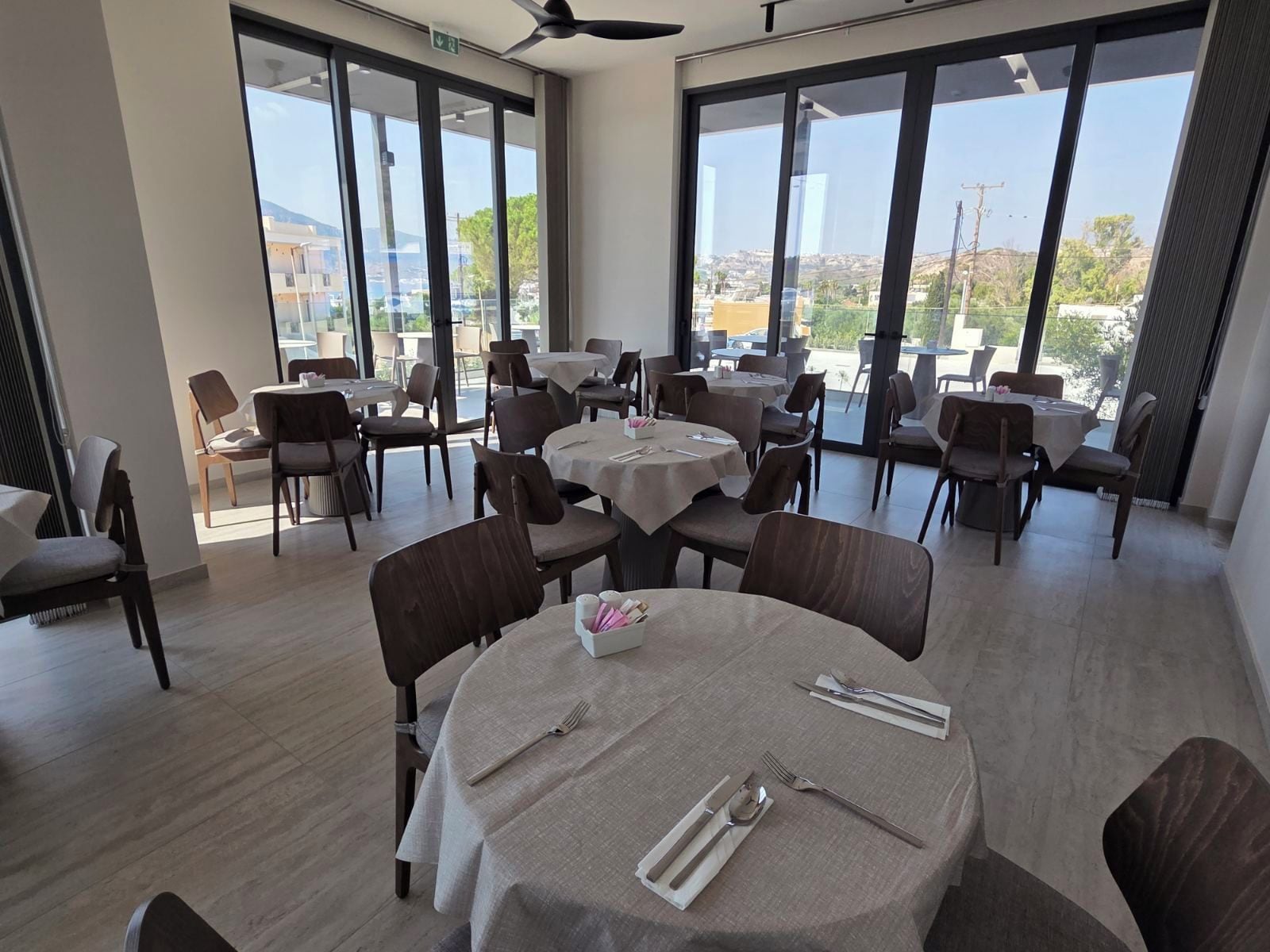 A restaurant with round tables, chairs, and a view of the city through large windows.