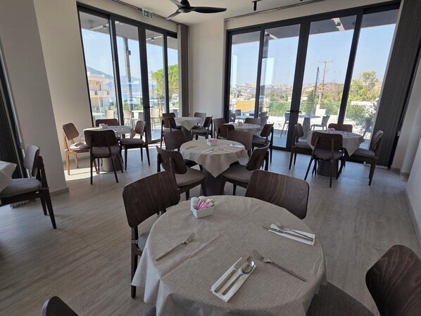 A restaurant with round tables, chairs, and a view of the city through large windows. - Kefalos View (Kos)