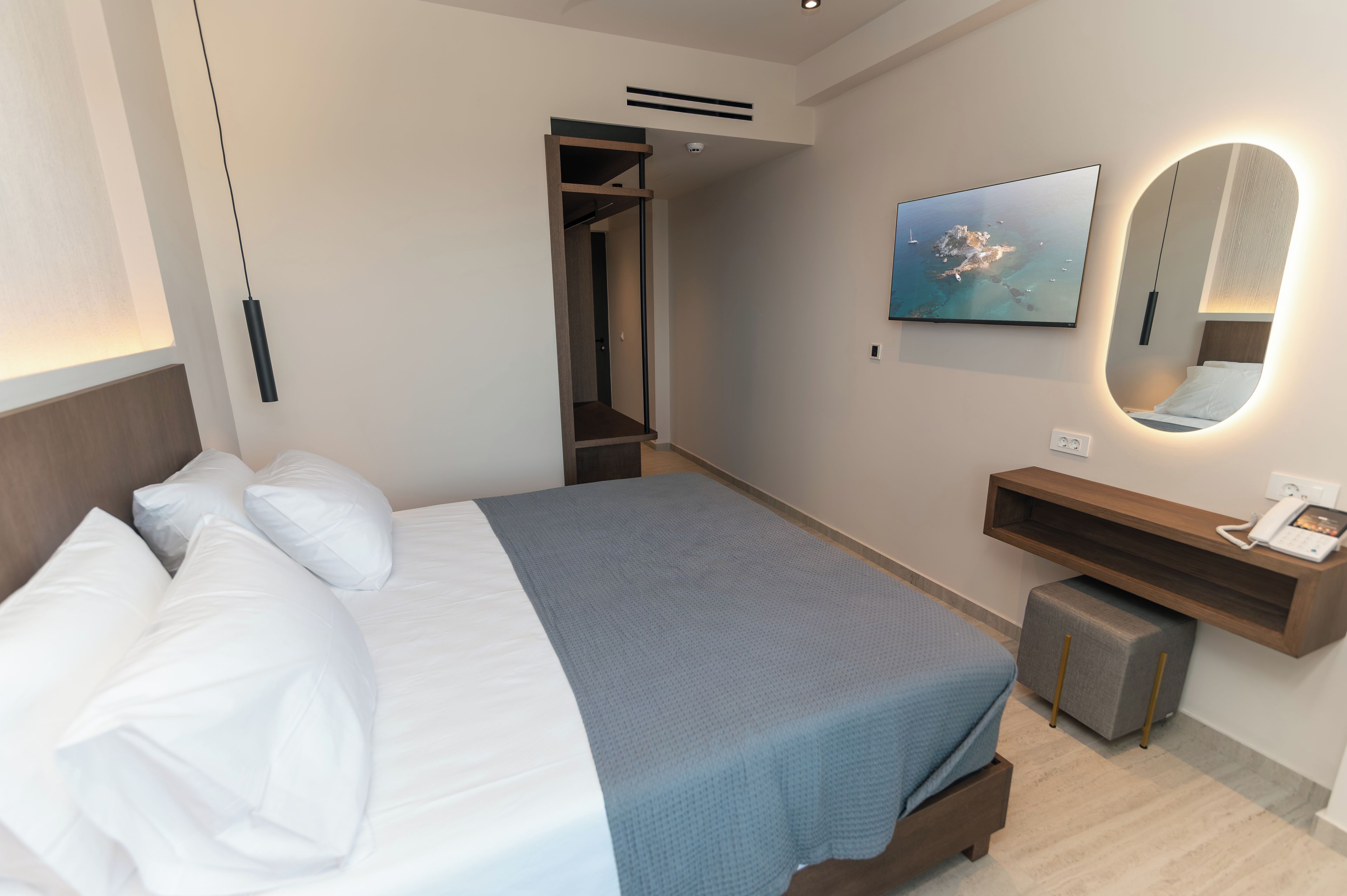 A hotel room with a bed, a bedside table with a phone, a mirror, and a painting of a coastal scene.