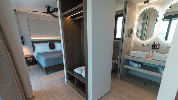 Quarto moderno com cama, guarda-roupa embutido e banheiro com pia e espelho.