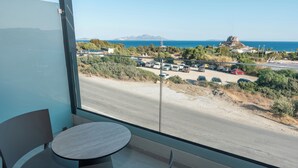 Uma varanda com vista para uma estrada costeira, carros estacionados e um afloramento rochoso ao longe.