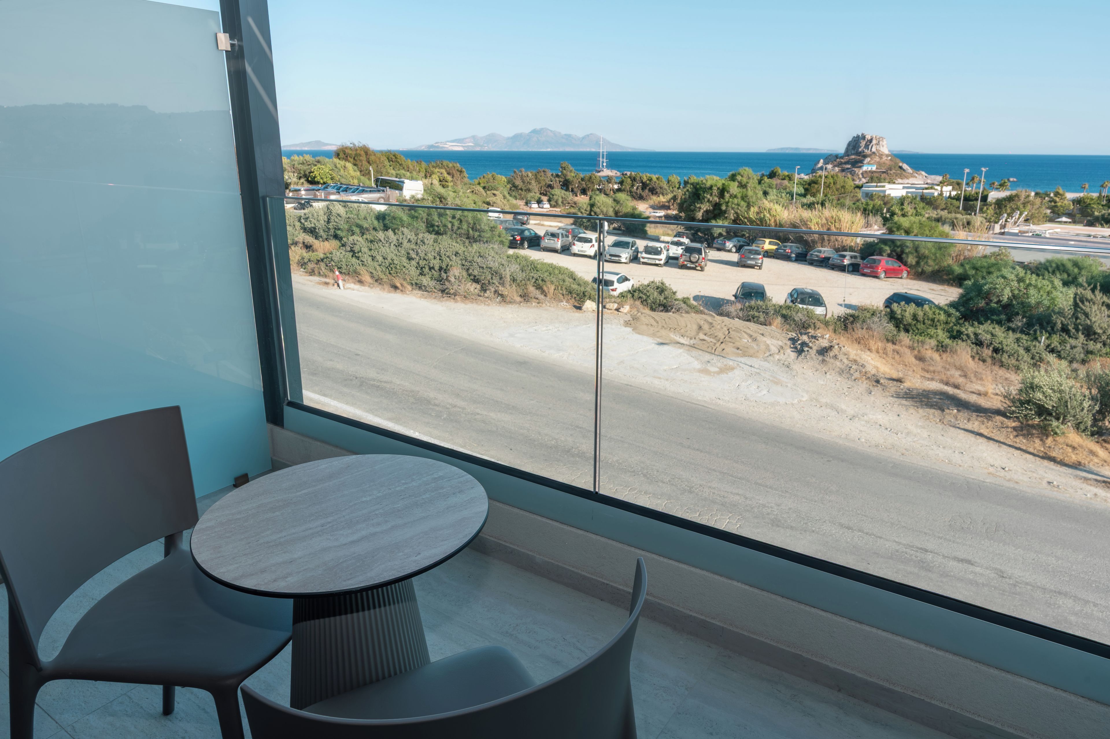 A balcony with a view of a coastal road, parked cars, and a distant rocky outcrop.
