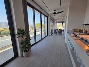 A modern hotel corridor with large windows, a ceiling fan, and a buffet area. - Kefalos View (Kos)