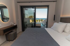 A hotel room with a bed, a desk with a telephone, a mirror, and a sliding glass door leading to a balcony with a view of the sea. - Kefalos View (Kos)