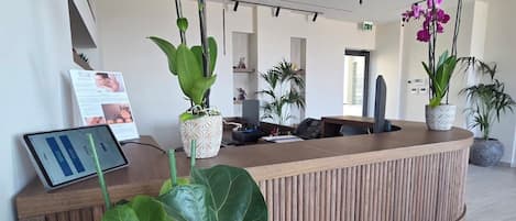 A reception desk with a modern design, surrounded by large green plants and purple orchids.