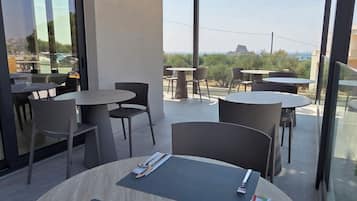 Een moderne buiten eethoek met ronde tafels en stoelen, uitzicht op zee, en een gebouw met grote ramen.