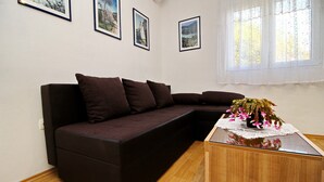 A living room with a dark brown sectional sofa, a wooden coffee table with a lace doily, and three framed pictures on the wall. - Apartments Nodilo - One Bedroom Apartment With Balcony and Sea View (Mljet)