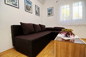 A living room with a dark brown sectional sofa, a wooden coffee table with a lace doily, and three framed pictures on the wall. - Apartments Nodilo - One Bedroom Apartment With Balcony and Sea View (Mljet)