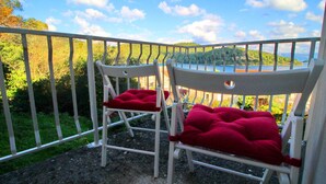 Two white chairs with red cushions on a balcony with a metal railing, overlooking a body of water and greenery. - Apartments Nodilo - One Bedroom Apartment With Balcony and Sea View (Mljet)
