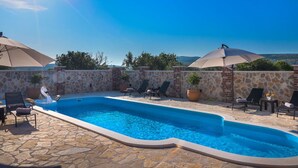 A swimming pool with lounge chairs and umbrellas, surrounded by stone walls and a clear sky. - Holiday Home Rider - Two Bedroom Holiday Home With Outdoor Pool (Sibenik)