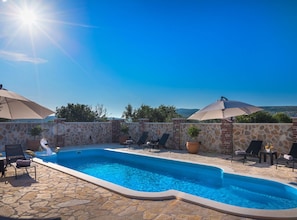 A swimming pool with lounge chairs and umbrellas, surrounded by stone walls and a clear sky. - Holiday Home Rider - Two Bedroom Holiday Home With Outdoor Pool (Sibenik)