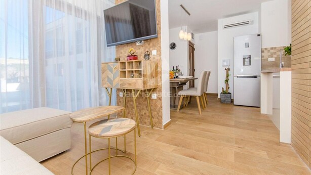 Een moderne woonkamer met een bank, een aan de muur bevestigde televisie en een eethoek met een tafel en stoelen.