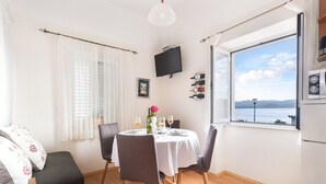 A dining area with a table set for two, a sofa, and a large window with a view of the sea. - Apartments Lotea - Two-bedroom Apartment With Terrace and Sea View (Konavle)