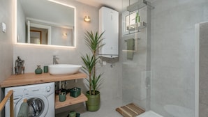 A modern bathroom with a built-in washing machine, a large mirror, a shower enclosure, and a wooden vanity. - Apartments Lotea - Two-bedroom Apartment With Terrace and Sea View (Konavle)