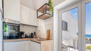 A modern kitchen with a built-in oven, a coffee maker, and a hanging plant shelf. - Apartments Lotea - Two-bedroom Apartment With Terrace and Sea View (Konavle)