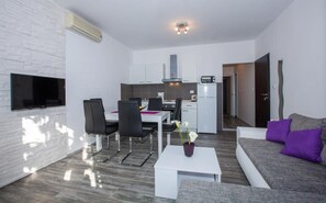 Ein modernes Wohnzimmer mit Flachbildfernseher, einem Essbereich mit Stühlen, einer Küche mit Schränken und einem Sofa mit Kissen.
