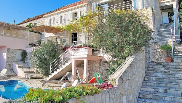 Un edificio de dos plantas con fachada de piedra, piscina y una escalera que lleva a un balcón.