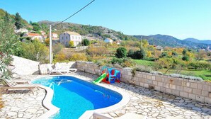 Una piscina con cubierta de piedra, sillas de descanso y un tobogán.