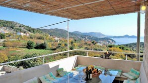 Un balcón con una mesa de vidrio, asientos y vistas a un paisaje montañoso.