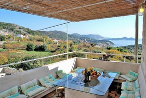 A balcony with a glass table, seating, and a view of a hilly landscape. - Villa Tony - Five Bedroom Villa With Terrace, Swimming Pool and Sea View (Dubrovnik)