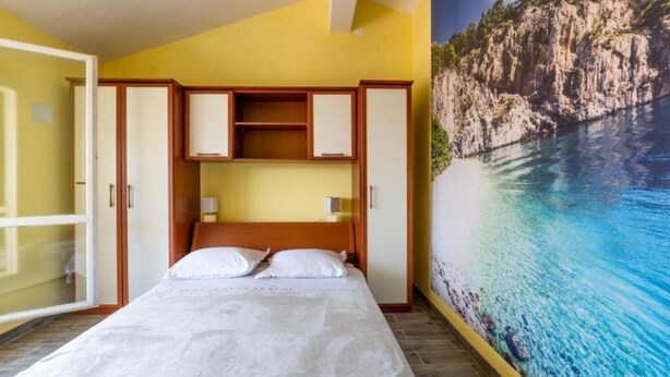 A hotel room with a bed, a wardrobe, a nightstand, and a mural of a coastal landscape. - Apartments Ribarevic - Studio With Balcony (Makarska)