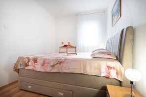 Ein Schlafzimmer mit einem Bett, einem Nachttisch, einer Lampe und einem Fenster mit Vorhängen.